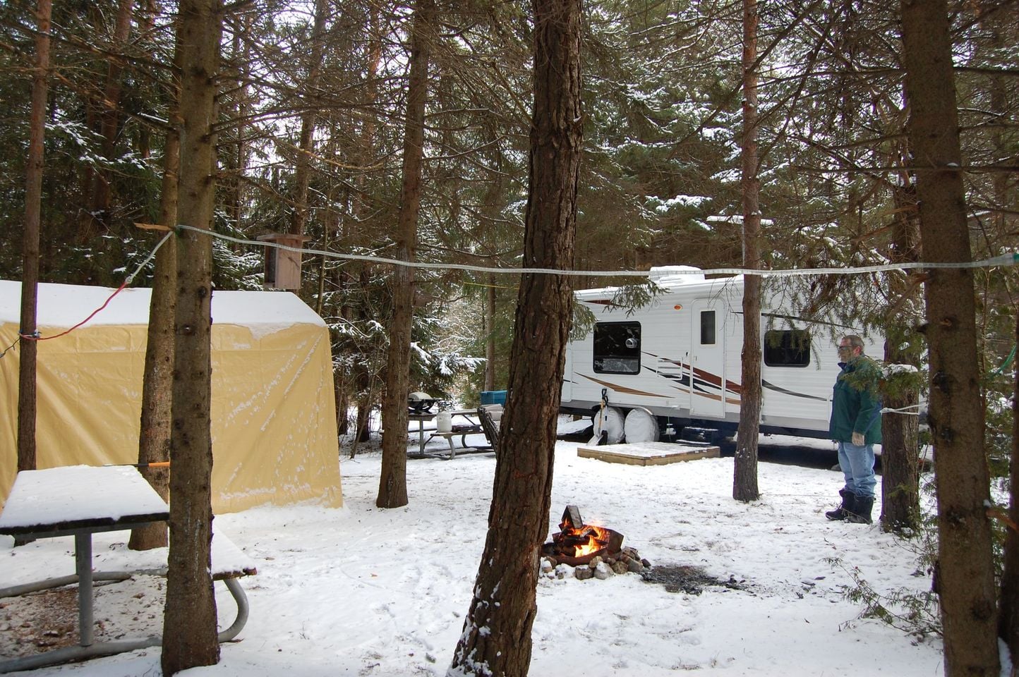 Winter camping, man beside trailer in forest